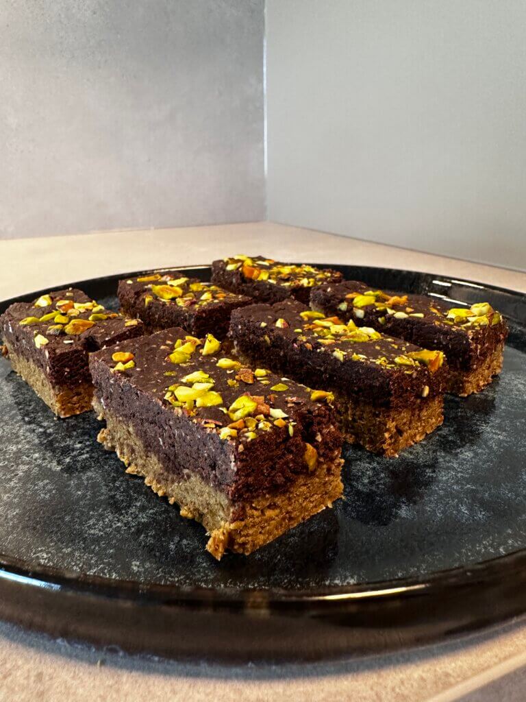 Gesunde Schoko-Pistazien-Schnitten auf schwarzem Teller – veganer Snack mit Nüssen und Schokolade